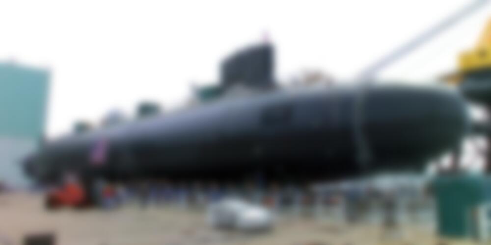 A long, black nuclear submarine suspended over a dock.