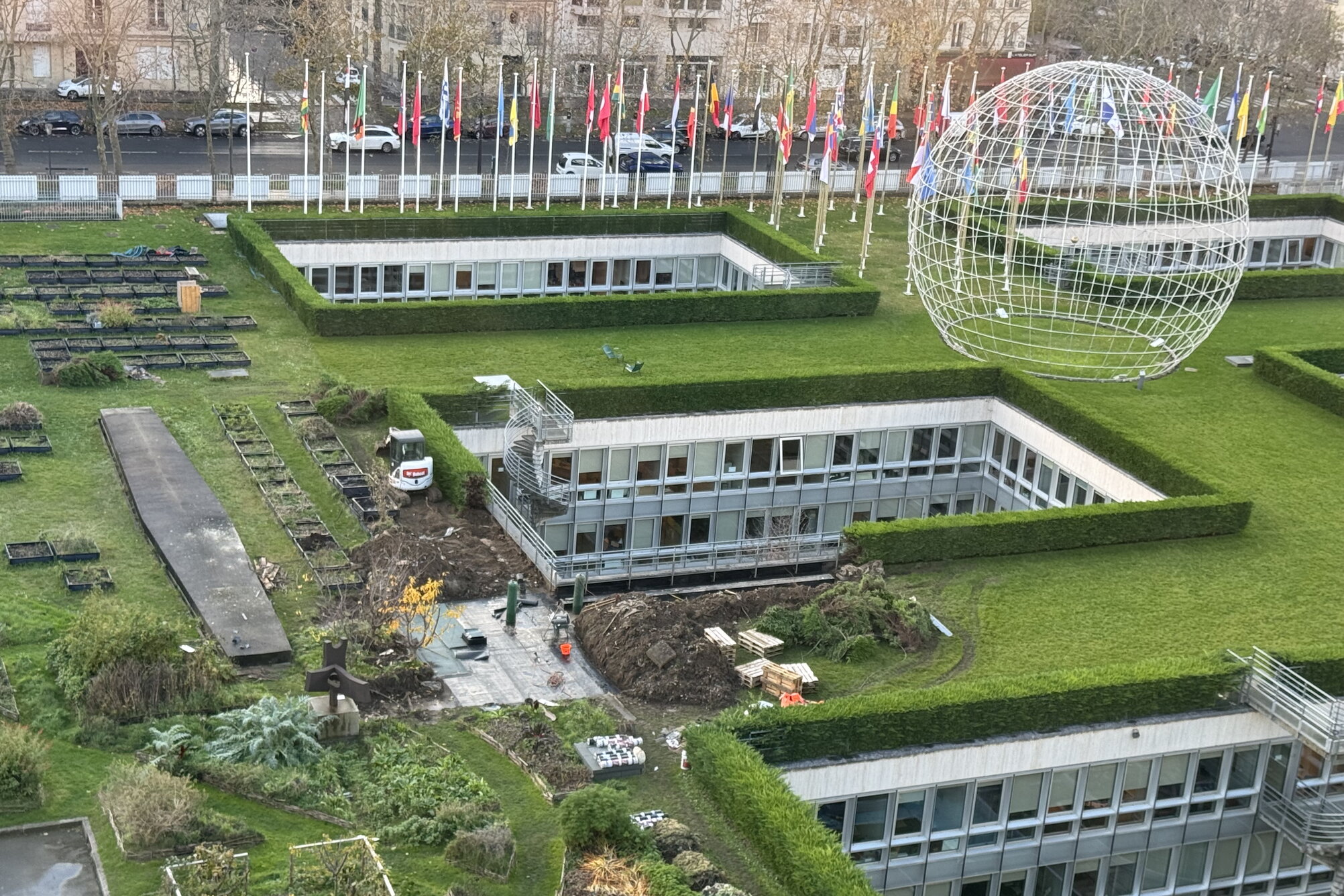 Top-down view of UNESCO headquarters with rooftop gardens, sculpture, and world flags.