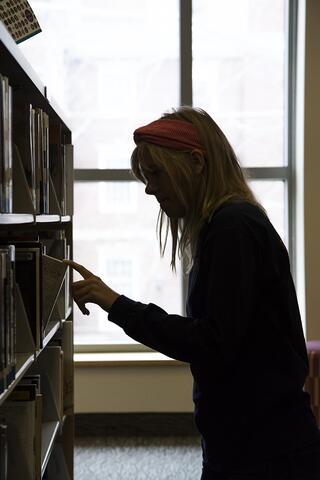 Photo of a woman picking a book off a shelf.